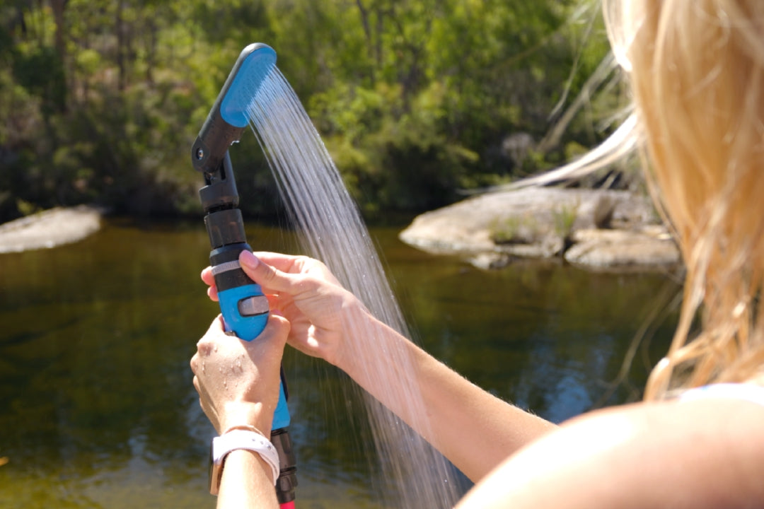 Person holding the HOTTAP Go adjustable showerhead, spraying water beside a river