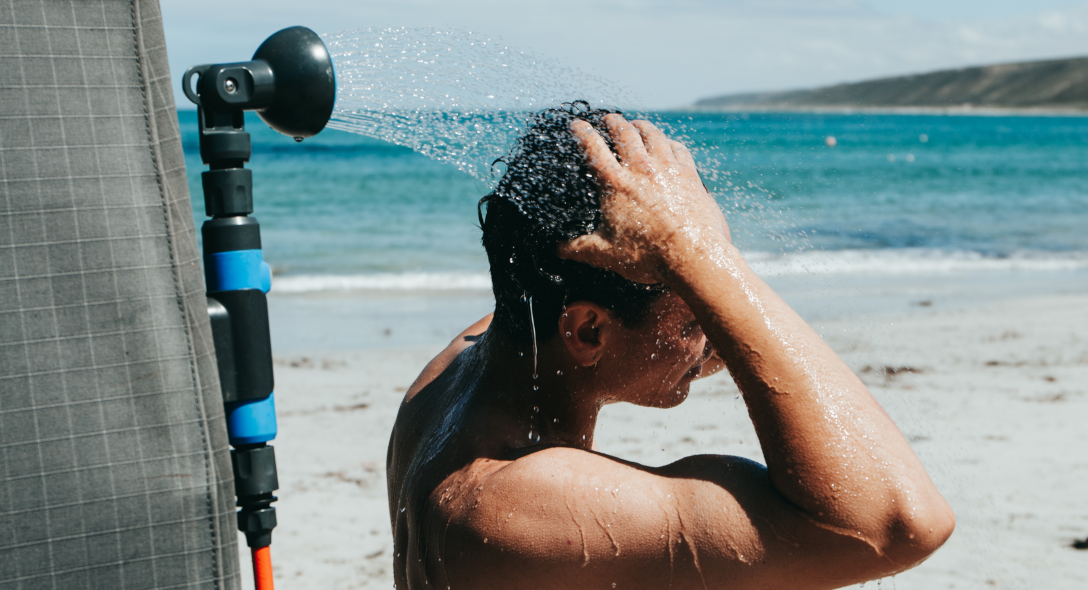 Man rinsing his hair under a camp shower by the beach