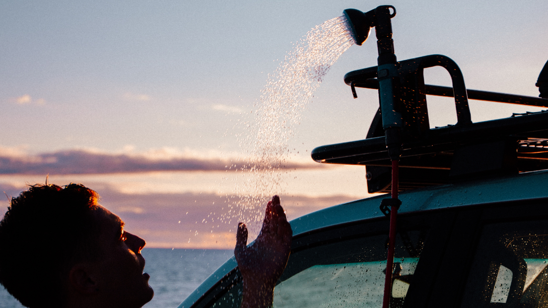 Person showering at sunset under a shower head on the side of a 4WD