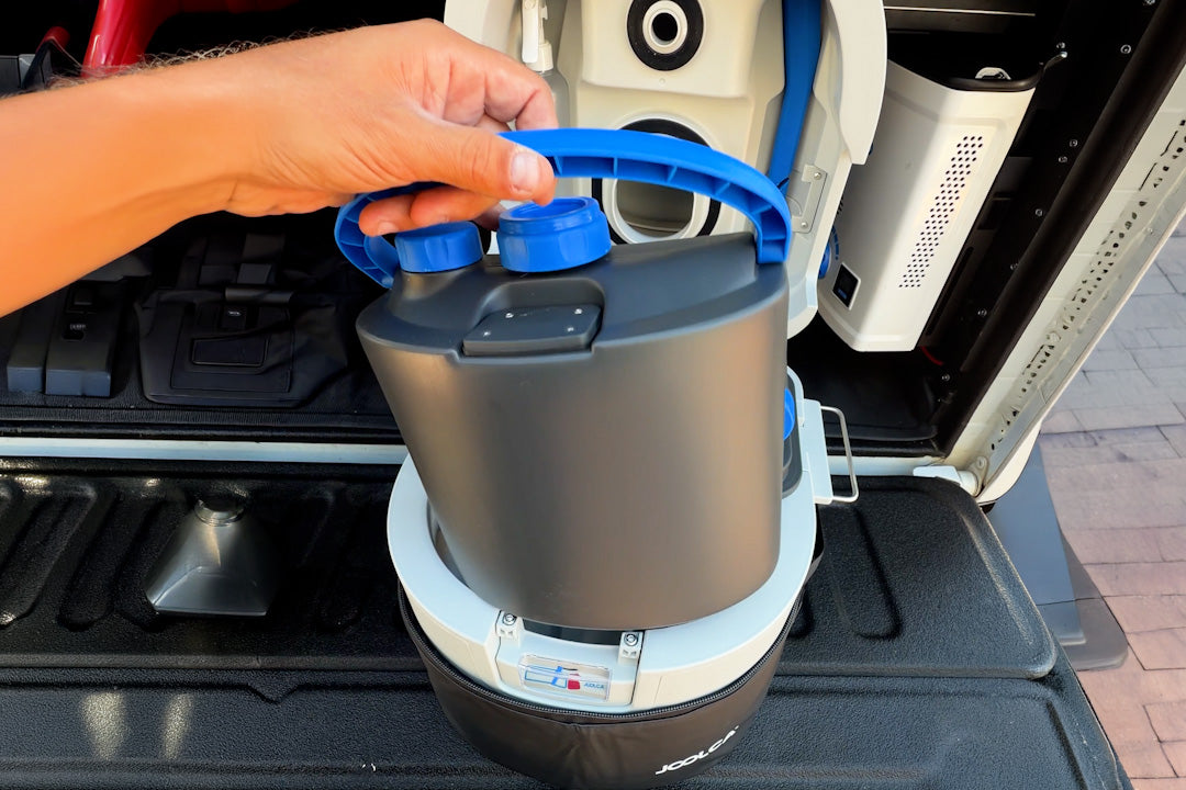Hand lifting the grey GottaGo urine container by its blue handle, inside a vehicle tray