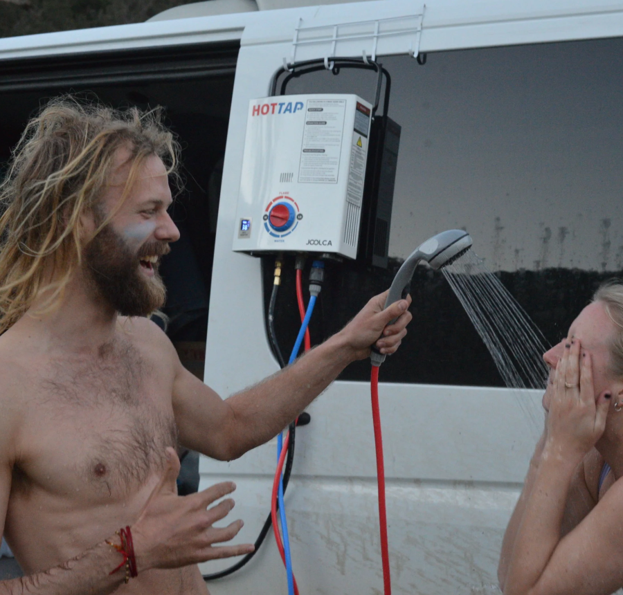 Two people using a portable shower attached to a vehicle, with a visible HOTTAP v1 unit.